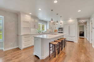 Kitchen with light wood-type flooring, sink, white cabinets, stainless steel double oven, and a kitchen island