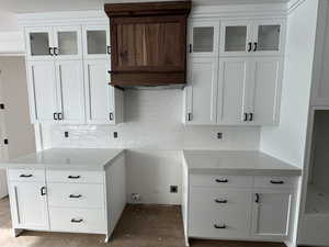 Kitchen with decorative backsplash, light stone countertops, and white cabinetry