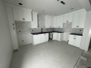 Kitchen with white cabinetry, backsplash, and sink