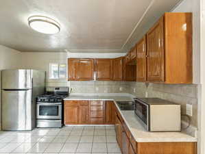 Kitchen featuring decorative backsplash, appliances with stainless steel finishes, and light tile patterned floors