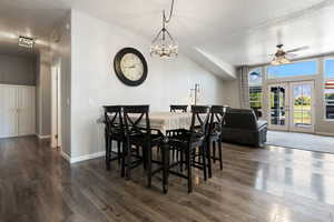 Dining space featuring vaulted ceiling, ceiling fan with notable chandelier, dark hardwood / wood-style flooring, a textured ceiling, and french doors