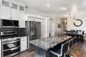 Kitchen with a kitchen island, dark wood-type flooring, white cabinetry, stainless steel appliances, and dark stone countertops