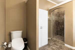 Bathroom with ornamental molding, tiled shower, tile patterned floors, and toilet