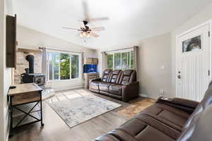 Living room with vaulted ceiling, ceiling fan, a wood stove, and plenty of natural light