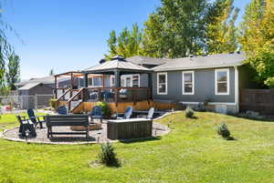 Back of house with a wooden deck, a patio area, an outdoor fire pit, and a yard