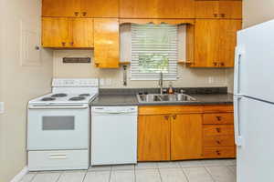 Kitchen with white appliances, electric panel, light tile patterned flooring, and sink