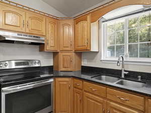 Kitchen featuring stainless steel range with electric cooktop, dark stone countertops, lofted ceiling, and sink