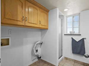 Laundry room with light tile patterned flooring, washer hookup, a textured ceiling, electric dryer hookup, and cabinets