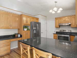 Kitchen featuring light hardwood / wood-style floors, stainless steel appliances, lofted ceiling, an inviting chandelier, and decorative light fixtures