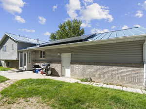 Rear view of house with a patio, a lawn, and solar panels