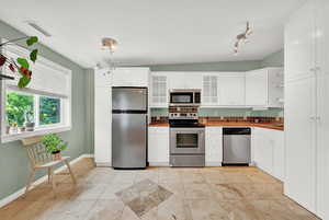 Kitchen featuring appliances with stainless steel finishes, light tile patterned floors, tasteful backsplash, and white cabinetry