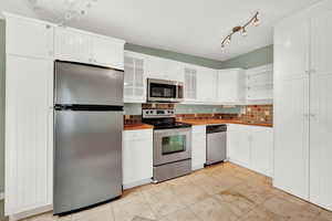 Kitchen with stainless steel appliances, backsplash, and white cabinetry