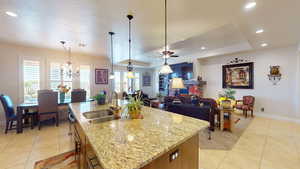 Kitchen featuring hanging light fixtures, an island with sink, light stone counters, a raised ceiling, and sink