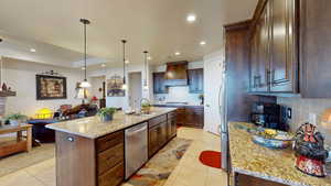 Kitchen with light stone counters, pendant lighting, stainless steel appliances, custom exhaust hood, and a kitchen island with sink