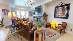 Tiled living room with ceiling fan, a raised ceiling, and a fireplace