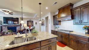 Kitchen featuring light stone counters, sink, custom range hood, a brick fireplace, and decorative light fixtures