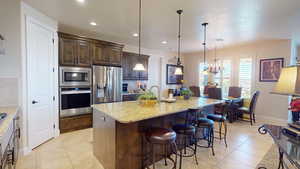 Kitchen featuring dark brown cabinetry, pendant lighting, a center island with sink, appliances with stainless steel finishes, and a breakfast bar area