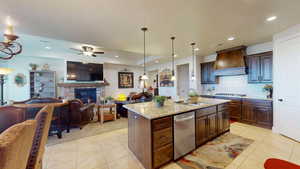 Kitchen featuring custom range hood, a fireplace, pendant lighting, a center island with sink, and sink