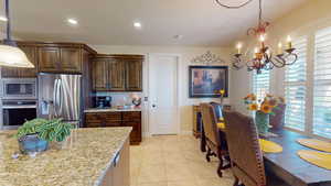 Kitchen with appliances with stainless steel finishes, light stone countertops, light tile patterned floors, pendant lighting, and an inviting chandelier