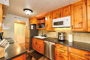 Kitchen with a textured ceiling, tasteful backsplash, sink, exhaust hood, and appliances with stainless steel finishes