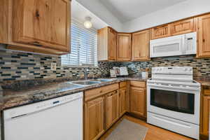 Kitchen with white appliances, backsplash, sink, and light wood-type flooring