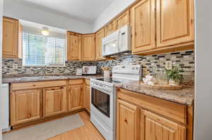 Kitchen with white appliances, tasteful backsplash, sink, and dark stone counters