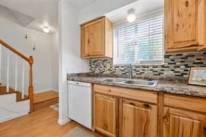 Kitchen featuring light brown cabinets, light hardwood / wood-style flooring, backsplash, white dishwasher, and sink