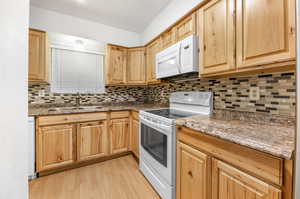 Kitchen with decorative backsplash, white appliances, light wood-type flooring, dark stone counters, and sink