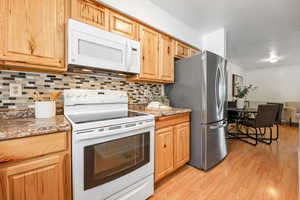 Kitchen featuring stone counters, light wood-type flooring, white appliances, and tasteful backsplash