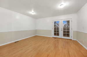 Spare room with french doors, a textured ceiling, crown molding, and light hardwood / wood-style floors