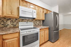 Kitchen with dark stone counters, light hardwood / wood-style flooring, backsplash, and white appliances