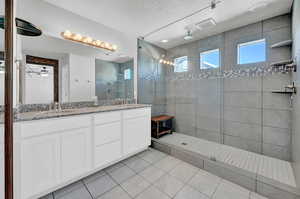 Bathroom featuring tile patterned flooring, upgraded tiled shower, vanity