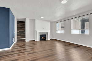 Unfurnished living room with a textured ceiling, a tiled fireplace, and dark wood-type LVP flooring