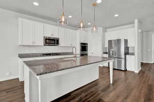 Kitchen with appliances with stainless steel finishes, dark hardwood / wood-style floors, sink, and white cabinets