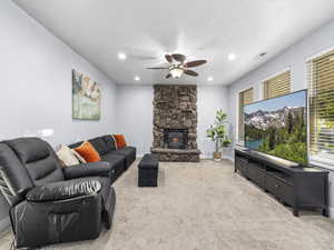 Carpeted living room with ceiling fan, a fireplace, and a textured ceiling