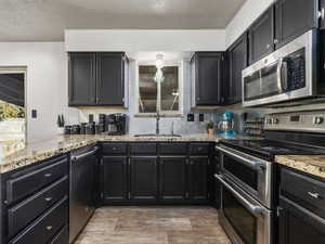 Kitchen with stainless steel appliances, a textured ceiling, light stone countertops, and sink