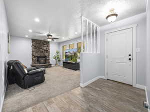 Living room featuring wood-type flooring, ceiling fan, a textured ceiling, and a stone fireplace