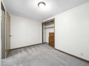 Unfurnished bedroom featuring light colored carpet, a textured ceiling, and a closet