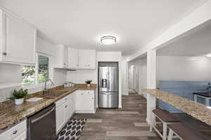 Kitchen with sink, white cabinetry, stainless steel appliances, dark stone counters, and dark hardwood / wood-style flooring