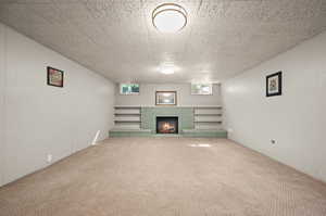 Unfurnished living room featuring a brick fireplace, carpet, and a textured ceiling