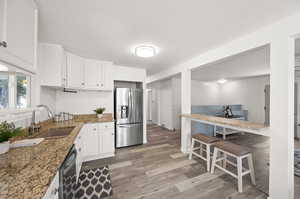 Kitchen with sink, white cabinetry, stone counters, stainless steel appliances, and hardwood / wood-style floors