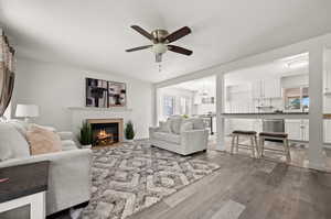 Living room featuring a tile fireplace, light hardwood / wood-style floors, ceiling fan with notable chandelier, and a wealth of natural light