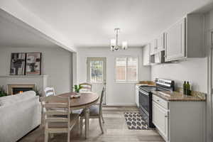 Kitchen with white cabinets, light wood-type flooring, decorative light fixtures, stainless steel electric stove, and a fireplace