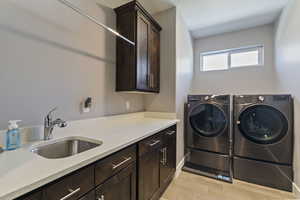 Laundry area with cabinets, light hardwood / wood-style floors, separate washer and dryer, and sink