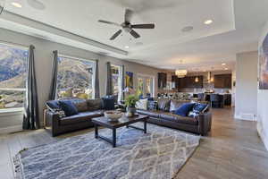 Living room with ceiling fan with notable chandelier, light wood-type flooring, and a raised ceiling