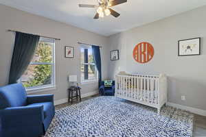 Bedroom featuring ceiling fan, a nursery area, and wood-type flooring