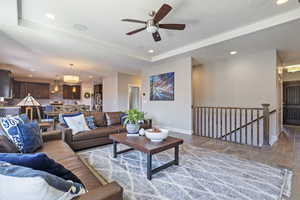 Living room with ceiling fan with notable chandelier, light wood-type flooring, and a tray ceiling