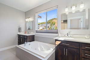 Bathroom with a relaxing tiled tub, vanity, and tile patterned flooring