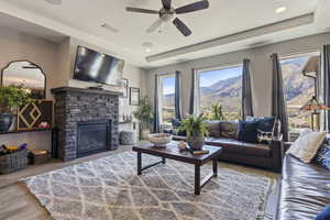 Living room featuring a raised ceiling, a stone fireplace, ceiling fan, and light hardwood / wood-style flooring