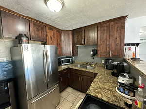 Kitchen with sink, dark brown cabinets, a textured ceiling, stainless steel appliances, and light stone countertops